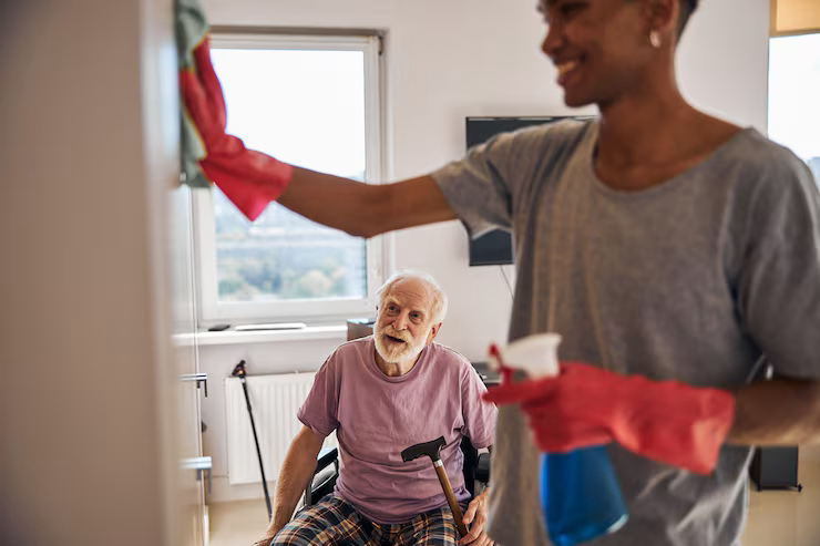 A Health Hive caregiver tidying the home of a smiling older man